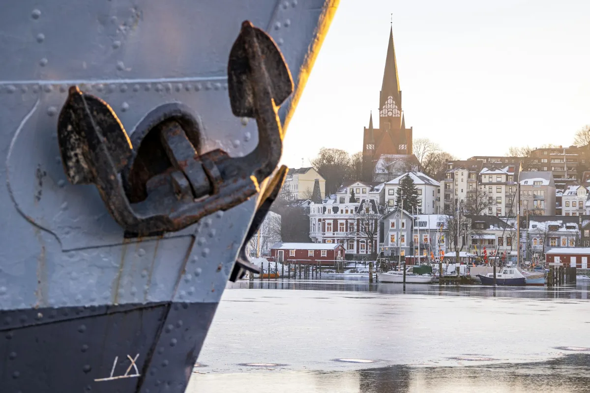 Et skibsanker i forgrunden med Flensborgs havn og kirketårn i baggrunden