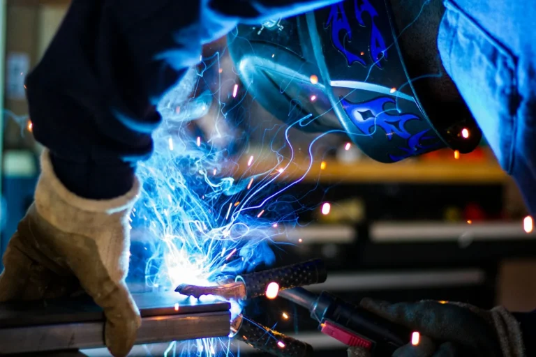 Svejser med beskyttelseshjelm arbejder på metal, mens gnisterne flyver